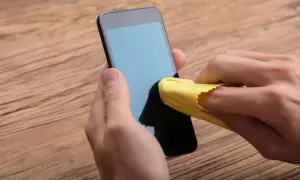 Main gauche tenant un téléphone, main droite utilisant un chiffon jaune pour nettoyer l'écran. Un geste simple pour nettoyer l'écran de votre téléphone.