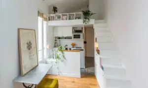 Petit appartement avec cuisine, bureau et escalier blanc menant à une mezzanine. Le placement en quinconce des étagères optimise l'espace.
