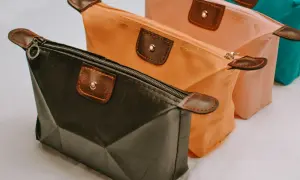 Trois trousses de maquillage colorées, dont une trousse silicone noire, orange et rose, avec des détails en cuir marron.