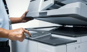 Main d'une personne appuyant sur les touches d'une imprimante, le couvercle ouvert pour vérifier la cartouche ou le réservoir.