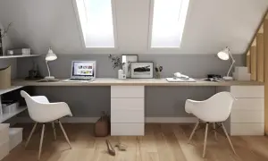 Deux bureaux modernes, dos à dos, sous des fenêtres de toit. L'espace de travail est lumineux et fonctionnel.