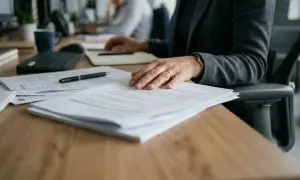 Main tenant sur des documents, une femme attend une réponse. Mon employeur refuse mon aménagement de poste, une situation stressante.