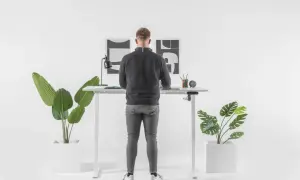 Un homme debout à un bureau réglable en hauteur. Il se demande combien de temps rester debout par jour pour un bien-être optimal.
