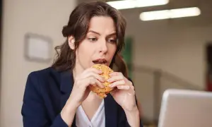 Une femme mange un hamburger à son bureau, profitant d'une pause déjeuner rapide.