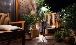 Ambiance chaleureuse sur une petite terrasse : deux chaises en bois, coussin, plaid, bougie et plantes vertes illuminées par des guirlandes.