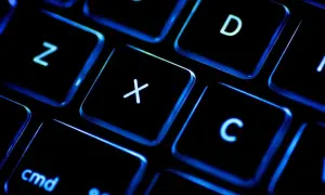 Gros plan sur un clavier rétroéclairé, les touches noires illuminées de bleu. On distingue les lettres Z, X, C, D et la touche "cmd". Un clavier BÉPO pour une frappe optimisée.