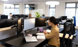 Une femme travaille à son bureau, entourée d'écrans. L'espace de travail semble bien organisé, suggérant une bonne gestion de la taille bureau m2.
