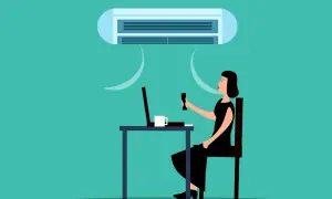 Une femme ajuste la climatisation de son bureau, cherchant la température idéale pour respecter le code du travail.