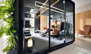 Une femme lit dans un bureau ouvert, un espace flex moderne avec une paroi végétale luxuriante et des cabines privées.