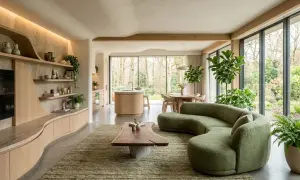 Salon aux formes organiques, inspiré par le biomimétisme. Canapé vert sinueux, table basse en bois brut, cuisine ouverte et vue sur la nature.
