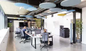 Des panneaux acoustiques colorés au plafond améliorent l'isolation acoustique du bureau. Des employés travaillent dans un espace moderne.