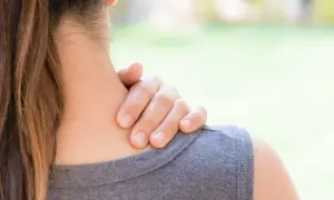 Une main masse la nuque d'une femme, suggérant un besoin d'échauffement cervicales après une longue journée.