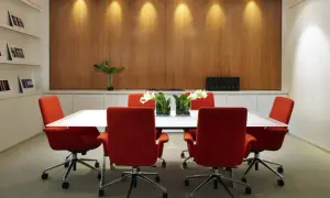 Salle de réunion moderne avec chaises rouges vives et une table blanche épurée. La décoration salle de réunion est complétée par des vases de fleurs et un mur boisé chaleureux.