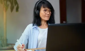 Femme avec casque et lunettes travaillant sur ordinateur portable, prenant des notes. Elle pratique le télétravail raison médicale.