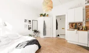 Chambre avec coin salon, lit blanc, cuisine ouverte et sol en bois clair. Décoration murale avec photos et affiche.