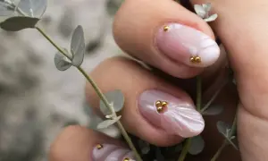 Manucure délicate aux perles dorées sur fond rose quartz, évoquant la douceur d'une fleur.