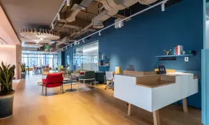 Un hall d'entrée d'entreprise moderne avec un bureau d'accueil blanc et bois, des fauteuils colorés et une grande fenêtre.