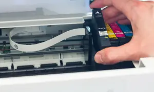 Main d'homme insérant une cartouche d'encre noire dans une imprimante. Il faut changer la cartouche pour continuer à imprimer.