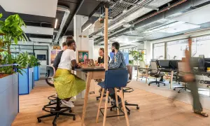 Aménagement bureau atelier : des collaborateurs échangent autour d'une table haute, dans un espace lumineux et végétalisé.