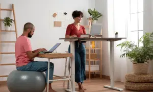 Un homme et une femme travaillent dans un bureau moderne. L'homme est assis sur un ballon de gym, la femme est en posture debout.
