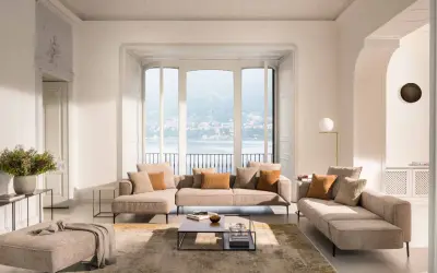 Salon lumineux avec canapé modulable, pouf et table basse, dans un style design scandinave épuré. Vue sur un lac.