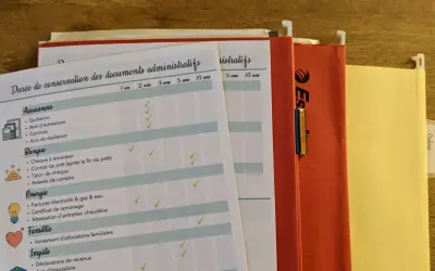 Tableau pour savoir comment ranger ses papiers : assurances, banque, énergie, famille, impôts. Dossiers suspendus orange et jaune.