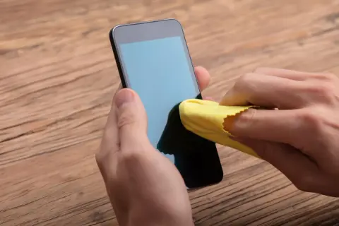 Main gauche tenant un téléphone, main droite utilisant un chiffon jaune pour nettoyer l'écran. Un geste simple pour nettoyer l'écran de votre téléphone.