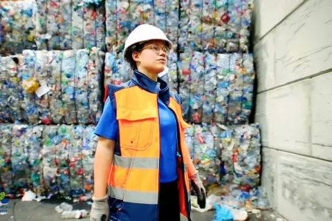 Employée en tenue de sécurité, devant des balles de plastique compressé. Elle veille au respect de la réglementation locale sur les déchets, en accord avec le code du travail.