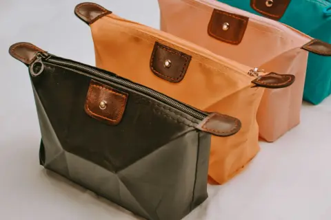 Trois trousses de maquillage colorées, dont une trousse silicone noire, orange et rose, avec des détails en cuir marron.