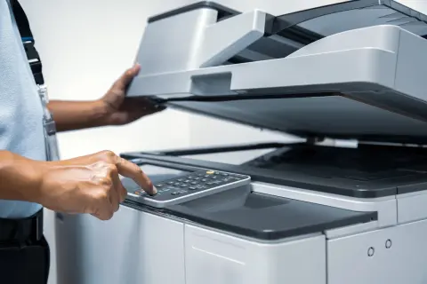 Main d'une personne appuyant sur les touches d'une imprimante, le couvercle ouvert pour vérifier la cartouche ou le réservoir.