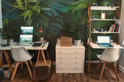 Un bureau chaleureux avec un mur végétal luxuriant, deux postes de travail équipés d'ordinateurs portables, des étagères remplies d'objets décoratifs et de livres, le tout sur un parquet en bois.