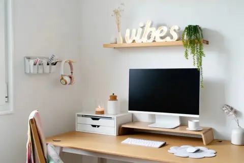 Un coin bureau fonctionnel pour un petit espace. Un bureau en bois avec un écran, un clavier, une souris, des écouteurs roses et une décoration murale "vibes".
