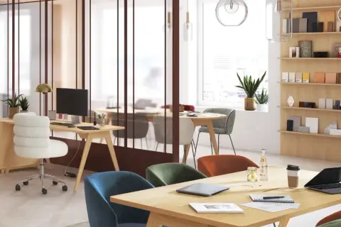 Aménagement espace coworking lumineux avec bureaux en bois, chaises colorées et étagères remplies d'échantillons.