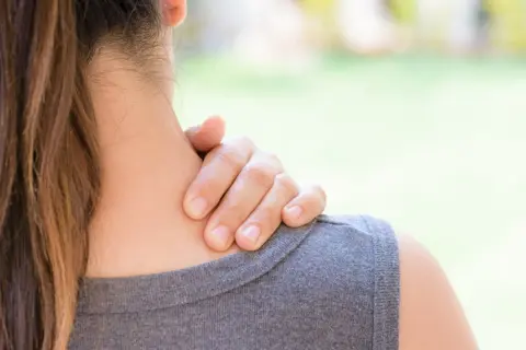 Une main masse la nuque d'une femme, suggérant un besoin d'échauffement cervicales après une longue journée.