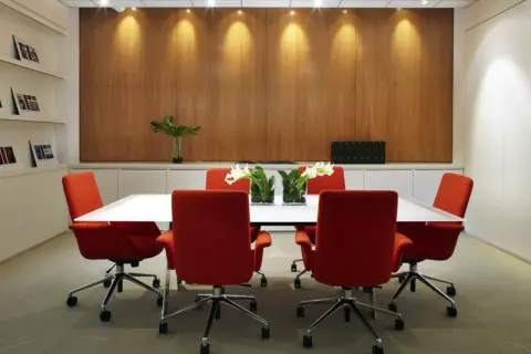 Salle de réunion moderne avec chaises rouges vives et une table blanche épurée. La décoration salle de réunion est complétée par des vases de fleurs et un mur boisé chaleureux.