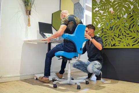 Un ergonome ou ergothérapeute ajuste un fauteuil bleu pour un homme travaillant sur un ordinateur portable.