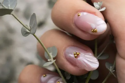 Manucure délicate aux perles dorées sur fond rose quartz, évoquant la douceur d'une fleur.