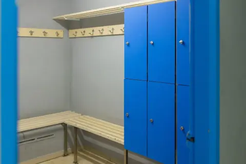 Vestiaire d'entreprise avec casiers personnels bleus, bancs en bois et patères.
