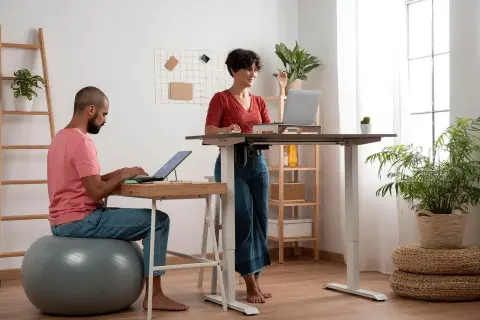 Un homme et une femme travaillent dans un bureau moderne. L'homme est assis sur un ballon de gym, la femme est en posture debout.