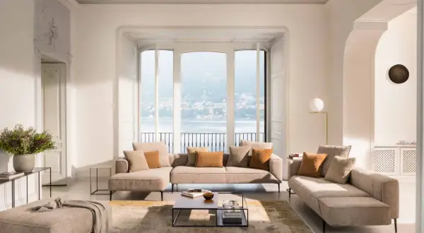 Salon lumineux avec canapé modulable, pouf et table basse, dans un style design scandinave épuré. Vue sur un lac.