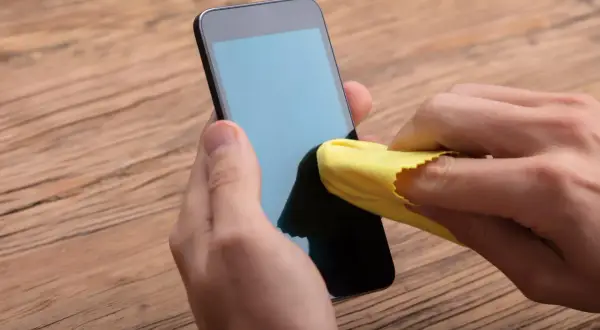 Main gauche tenant un téléphone, main droite utilisant un chiffon jaune pour nettoyer l'écran. Un geste simple pour nettoyer l'écran de votre téléphone.