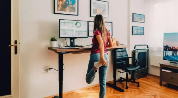 Femme s'étirant à son bureau réglable en hauteur, profitant du confort au bureau avec ses deux écrans.
