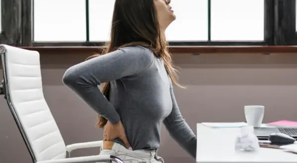 Femme souffrant de mal de dos, possiblement une hernie discale, à cause du travail assis.