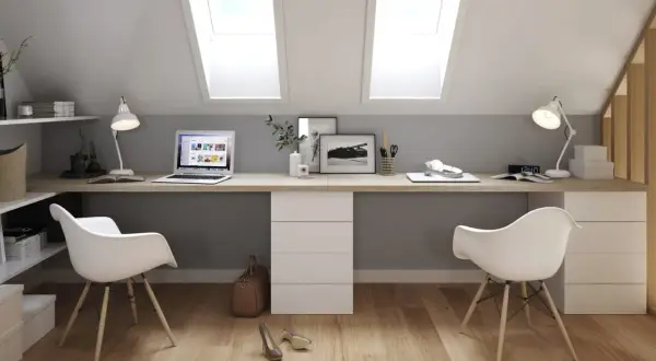 Deux bureaux modernes, dos à dos, sous des fenêtres de toit. L'espace de travail est lumineux et fonctionnel.