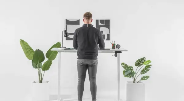 Un homme debout à un bureau réglable en hauteur. Il se demande combien de temps rester debout par jour pour un bien-être optimal.