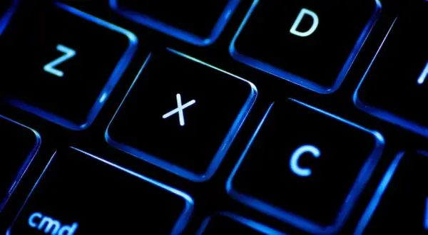 Gros plan sur un clavier rétroéclairé, les touches noires illuminées de bleu. On distingue les lettres Z, X, C, D et la touche "cmd". Un clavier BÉPO pour une frappe optimisée.