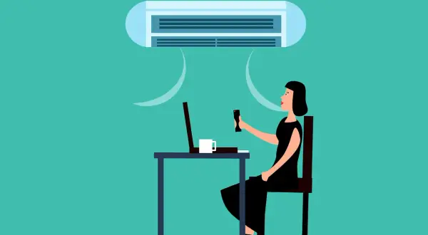 Une femme ajuste la climatisation de son bureau, cherchant la température idéale pour respecter le code du travail.