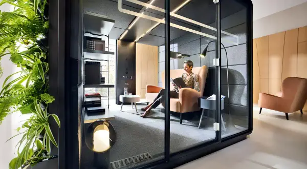 Une femme lit dans un bureau ouvert, un espace flex moderne avec une paroi végétale luxuriante et des cabines privées.