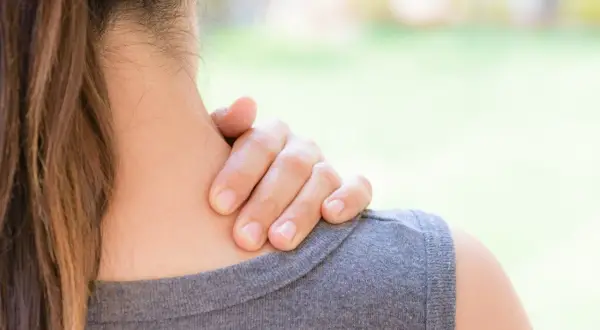 Une main masse la nuque d'une femme, suggérant un besoin d'échauffement cervicales après une longue journée.