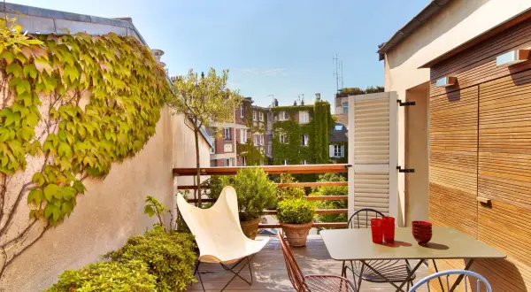 Une belle idee amenagement terrasse : mobilier coloré, plantes luxuriantes et vue sur les toits. Parfait pour un moment de détente.